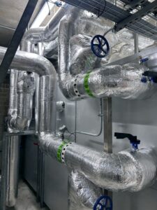 Industrial pipework with isolation valves, pumps and heat exchanger insulated with foiled fiberglass by Lagforce